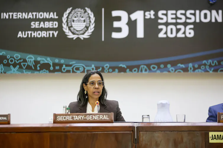 Image of a middle aged woman wearing glasses sat behind a desk speaking. There is a plaque that says Secretary-General in front of her, and a banner behind her reading International Seabed Authority 31st Session 2026.