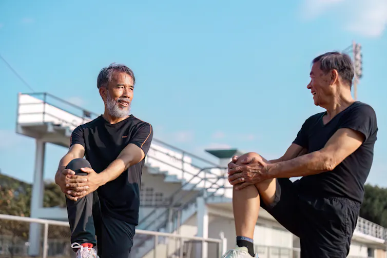 Two brothers or friends stretch their legs together before exercising.