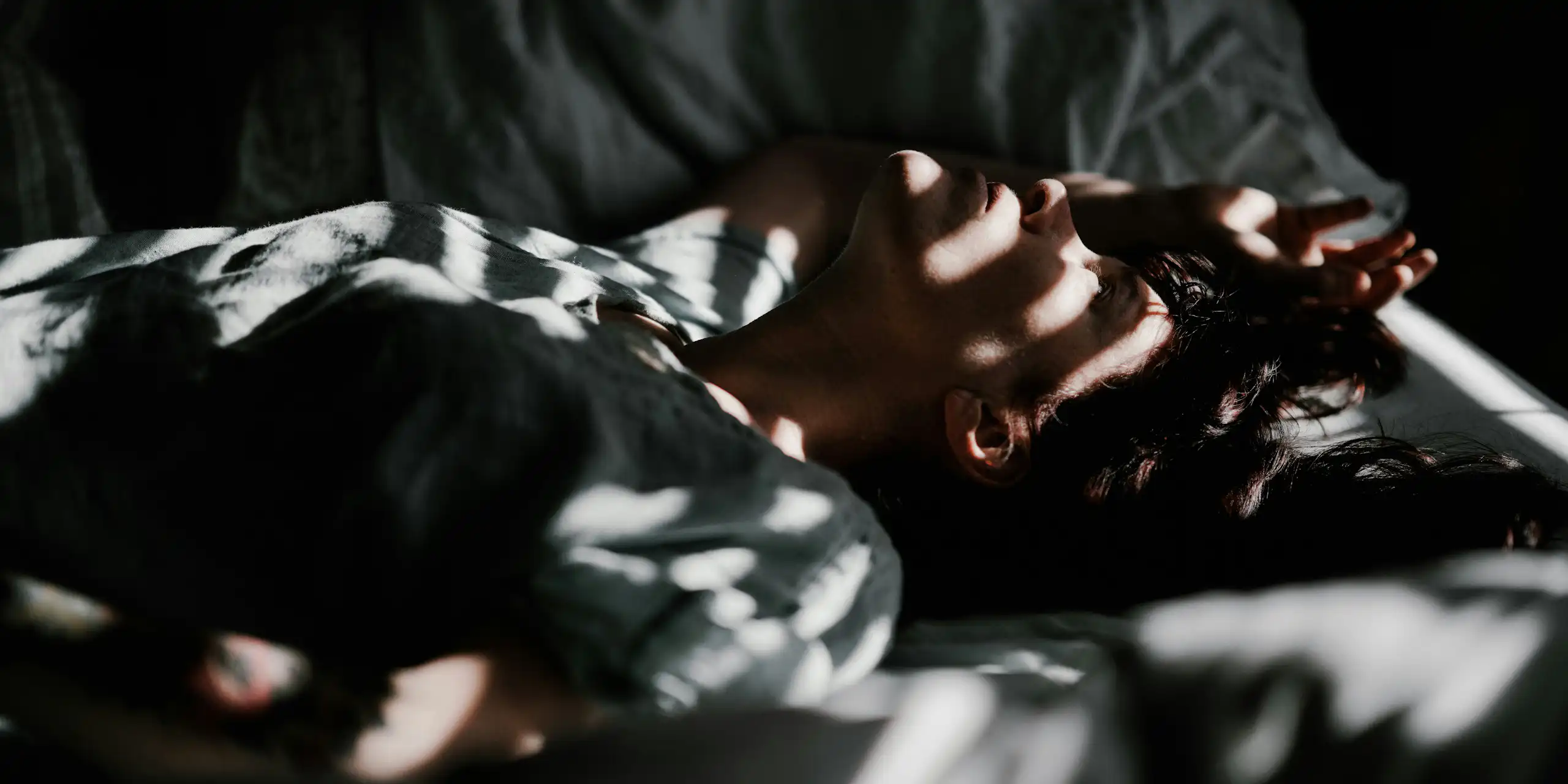 Un homme est couché dans un lit dans la pénombre.