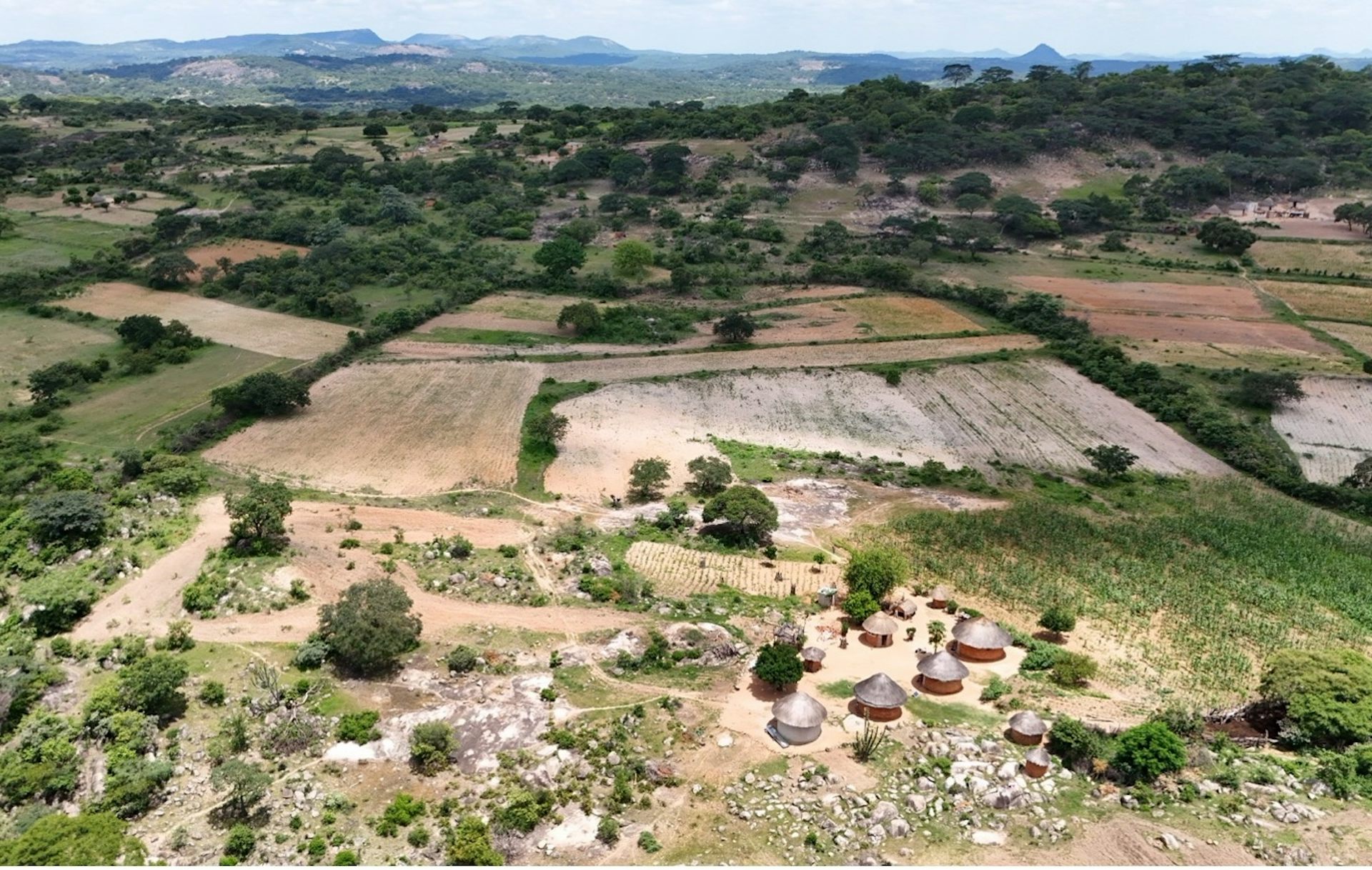 A vast landscape with huts, farming fields and mountains in the distance.