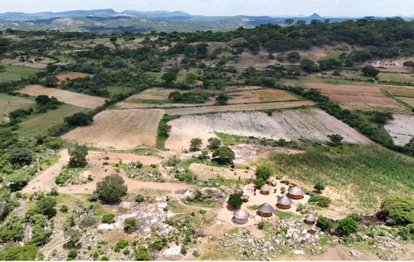A vast landscape with huts, farming fields and mountains in the distance.