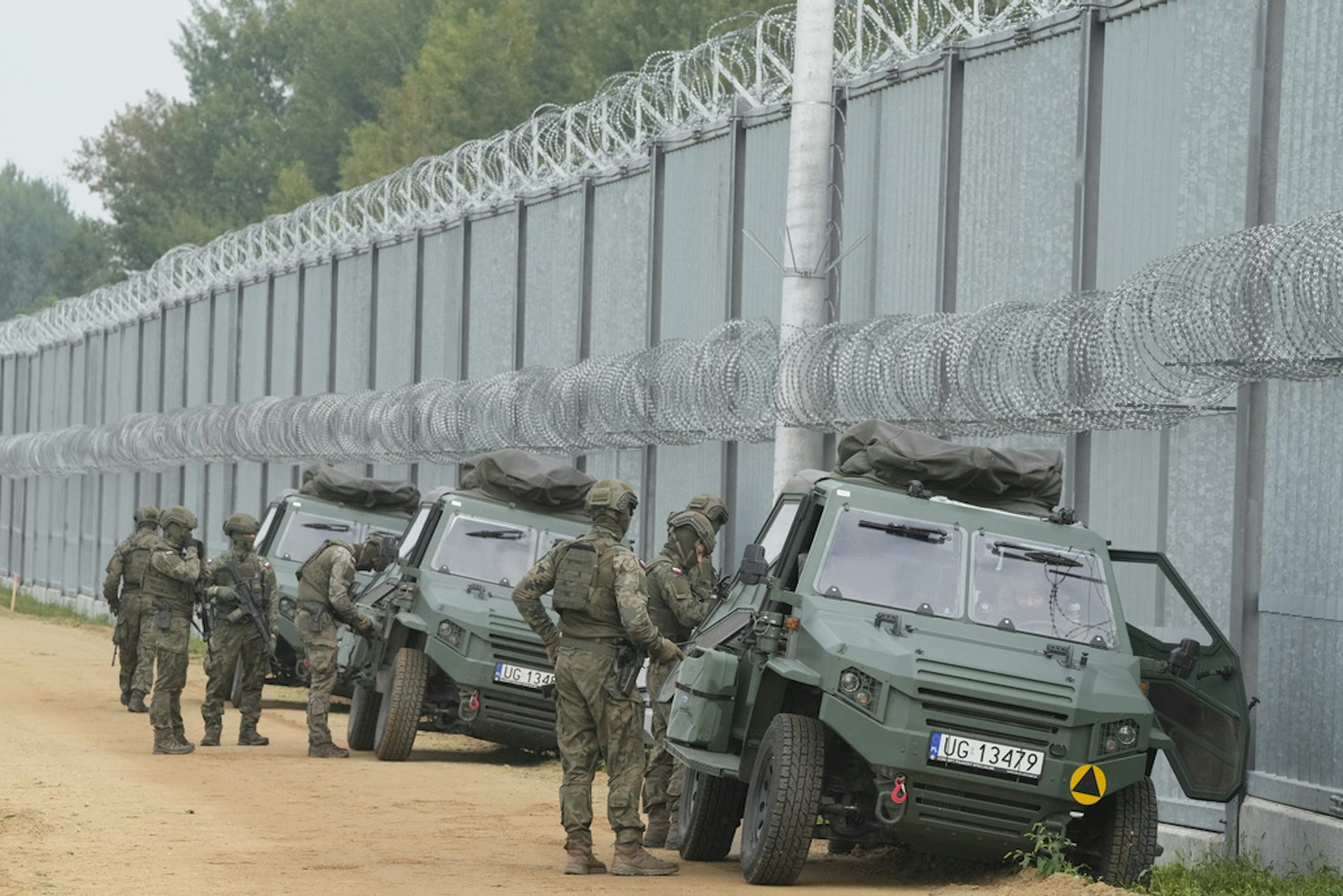 Soldiers stands next to a securitized border wall.