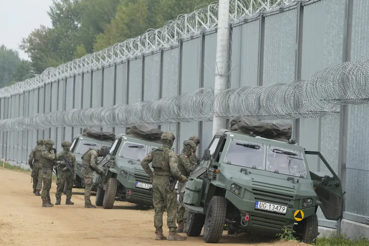 Soldiers stands next to a securitized border wall.