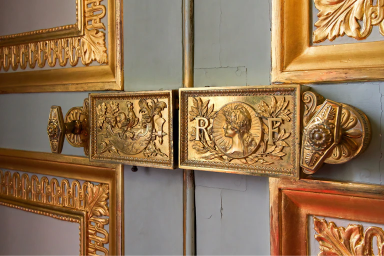 Les lambris de l’Élysée : gros plan sur les verrous plaqués or sculptés à l'effigie de la République française.