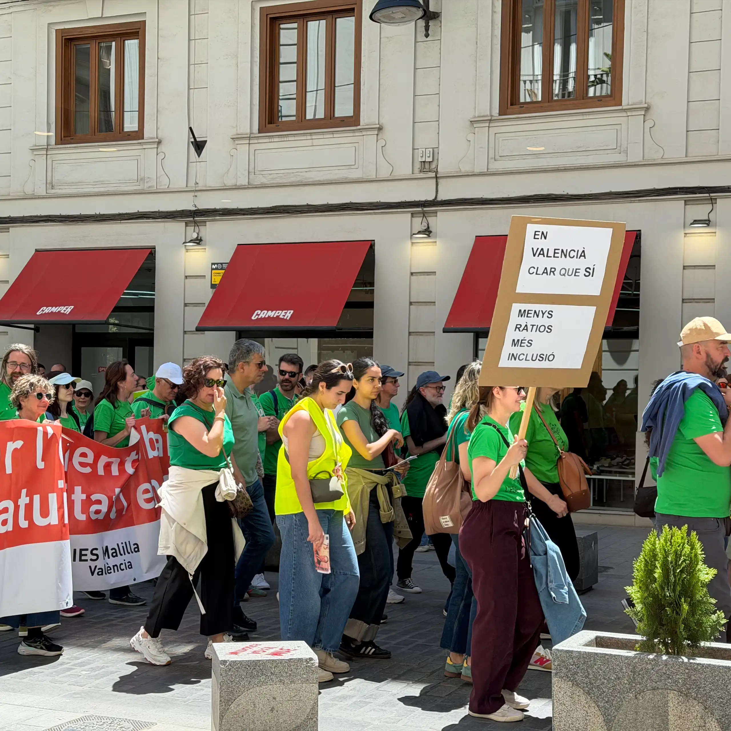 Gent vestida amb una samarreta verda al carrer. Porten un cartell on es llig: "Més ràtios, més inclusió".