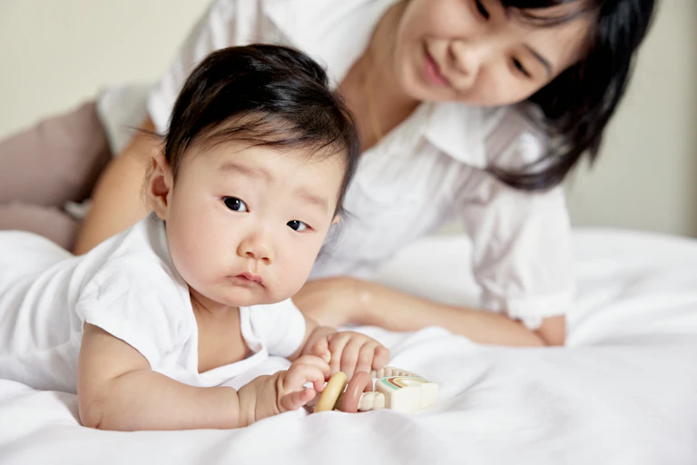 A woman and an infant are lying down together on a bed.