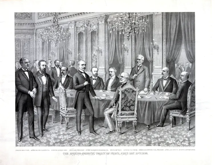Pictured are several people in suits standing around a table