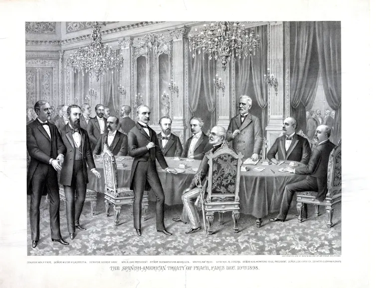 Pictured are several people in suits standing around a table