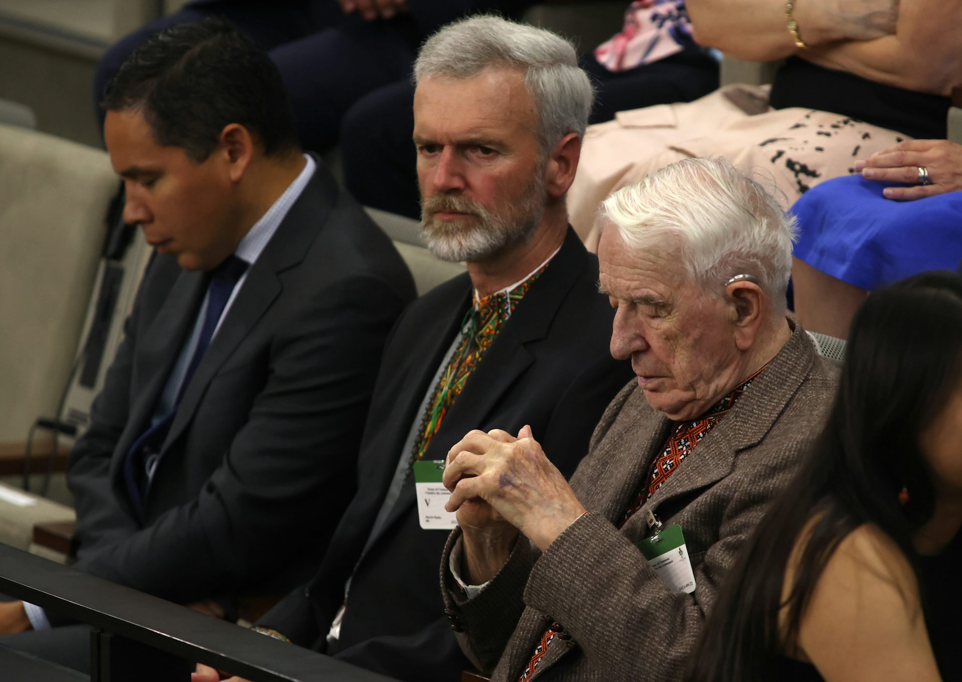 An elderly white man with white hair in a brown suit sits with his head bowed