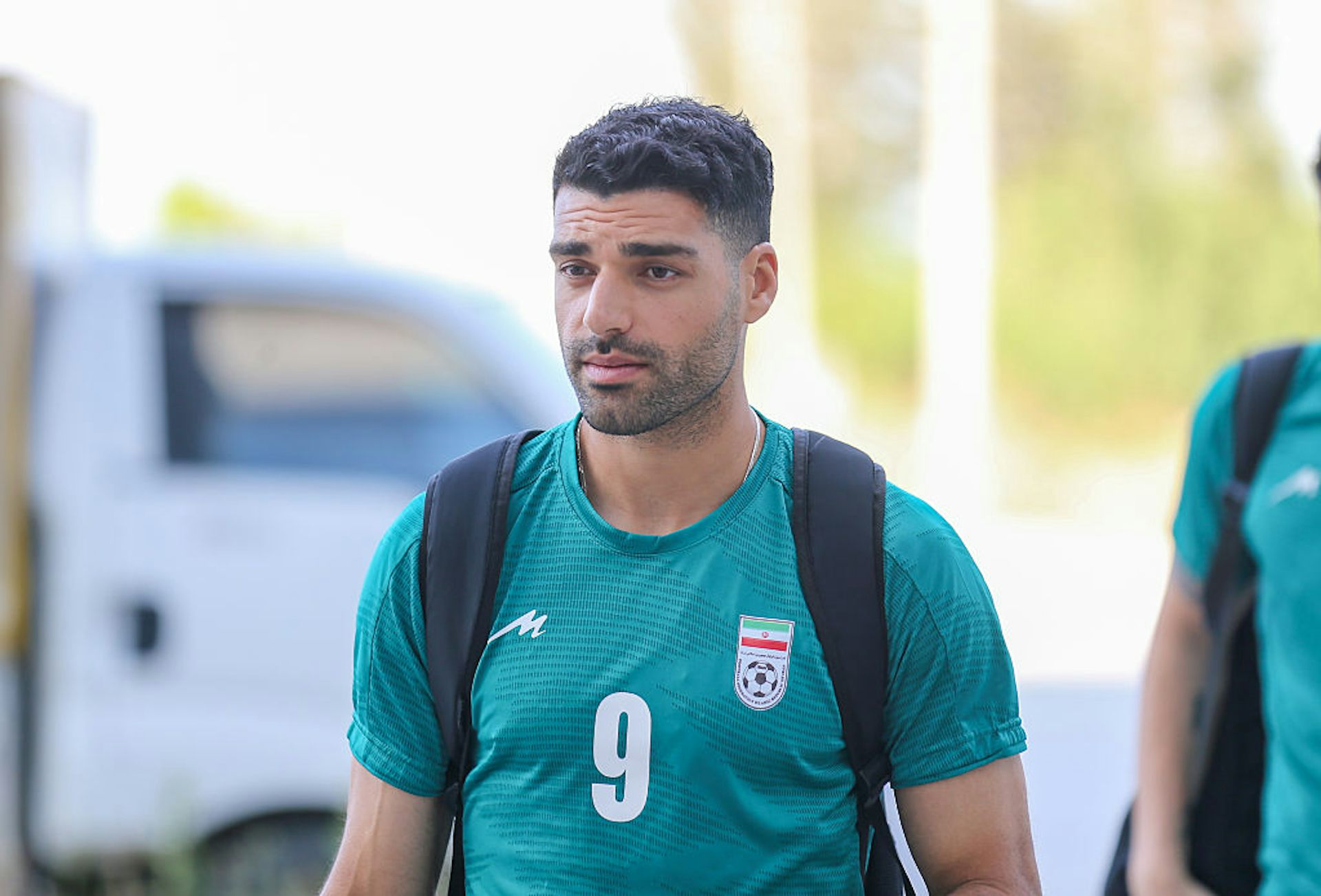 Young Middle Eastern man wearing a green, dry-fit shirt and a backpack.