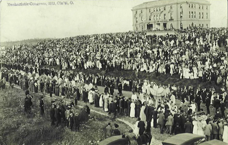 Cincinnati, donde Vance se convirtió, ofrece una visión de la historia del catolicismo en el corazón de Estados Unidos. 2 Fotografía en blanco y negro de una gran multitud parada a lo largo de una carretera con un gran edificio blanco al fondo.