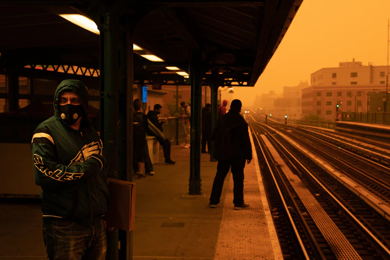 People stand on a train platform in very smoky, orange air.