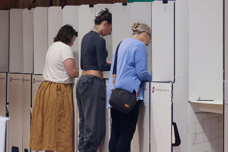 Three women in cardboard polling booths cast their votes