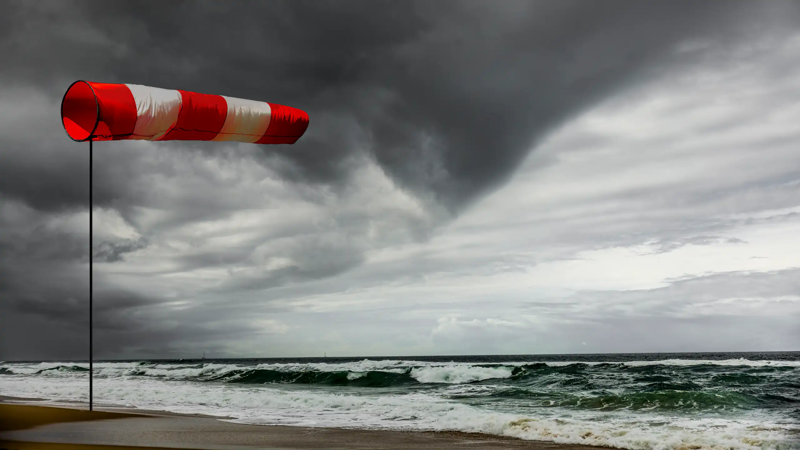 a windsock full of wind next to stormy ocean, dark clouds.