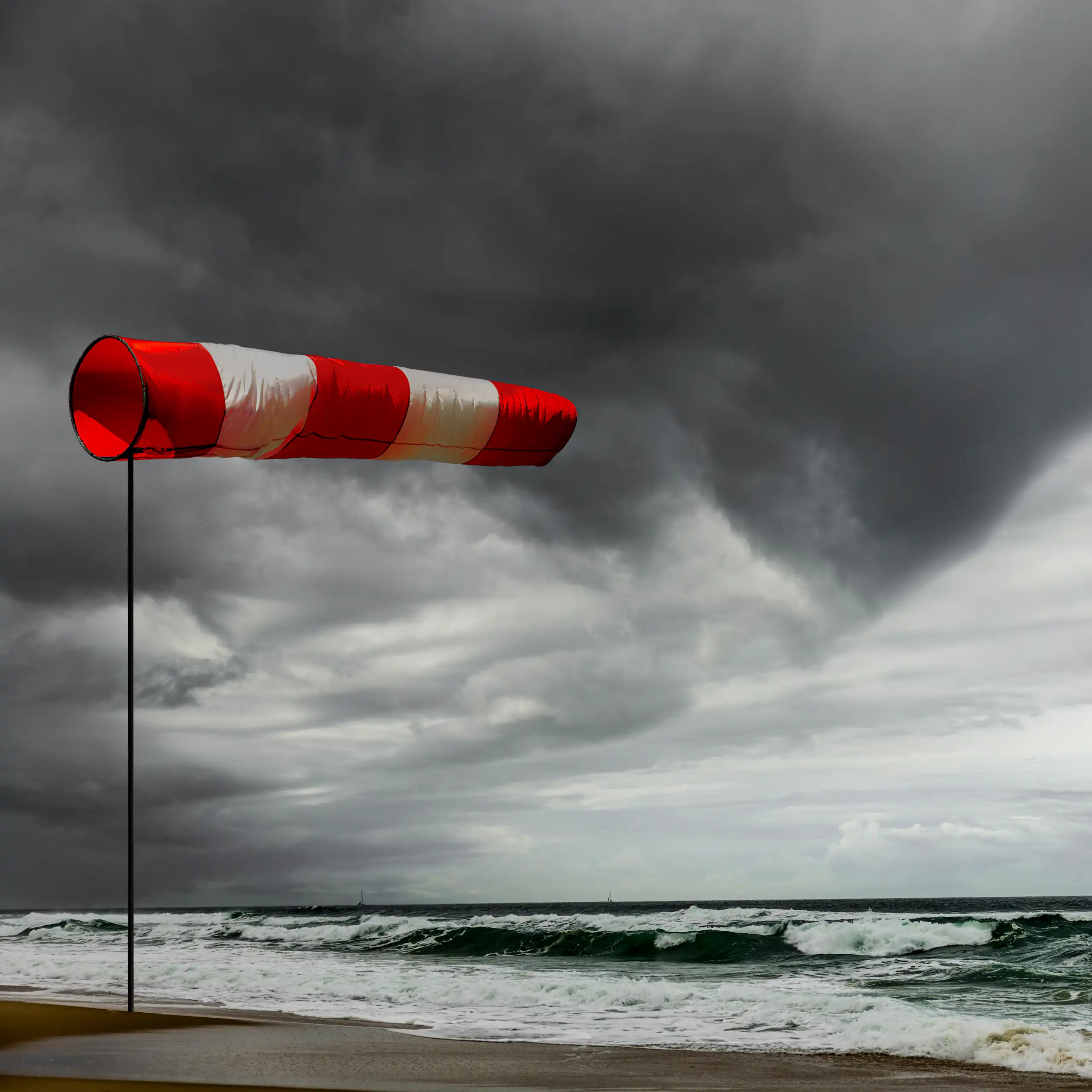 a windsock full of wind next to stormy ocean, dark clouds.