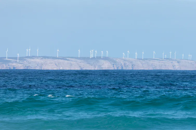 wind farm in background, blurry, and choppy ocean waves, dark blue ocean in foreground.