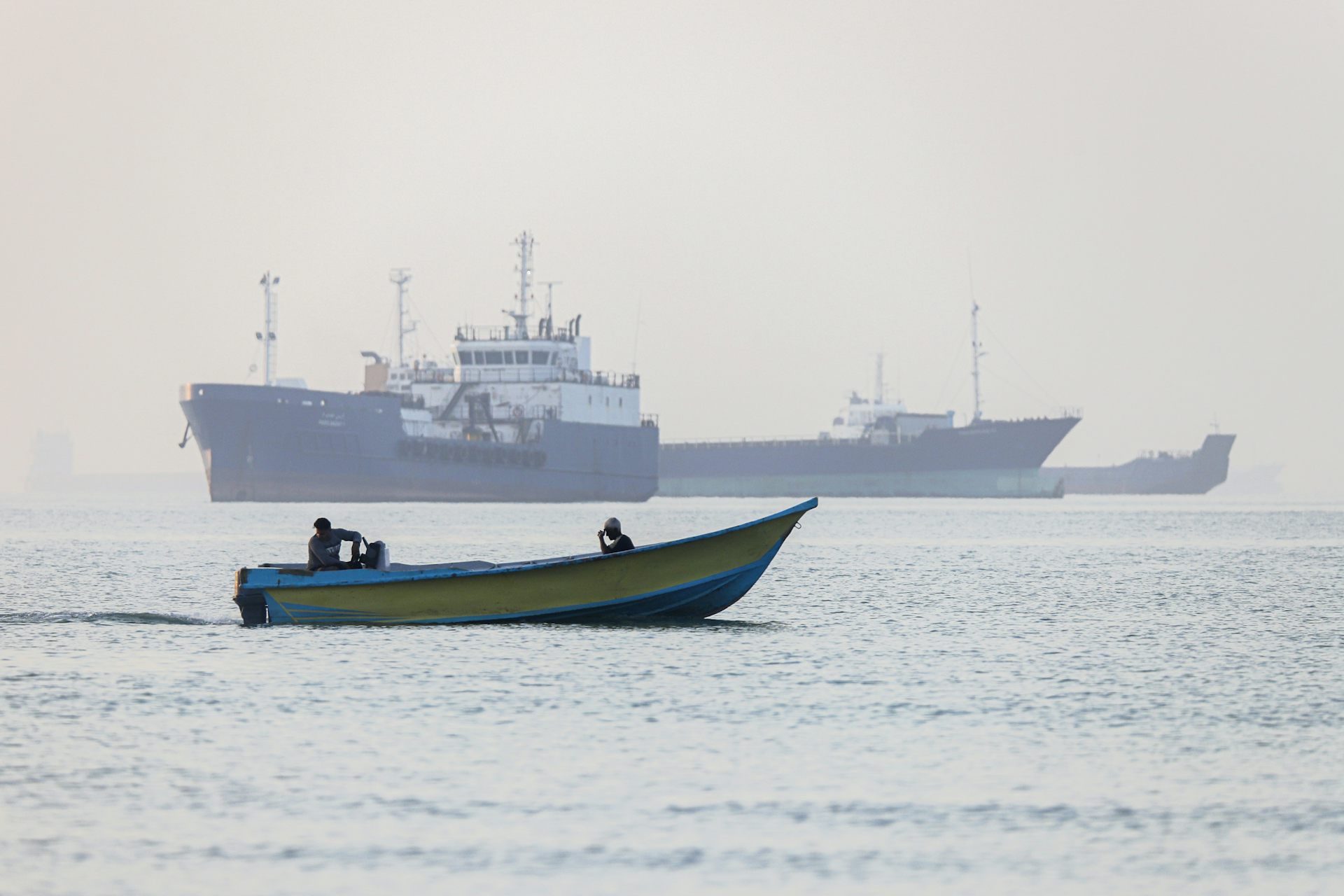 Iranian fishermen steering a boat past ships stuck in the Strait of Hormuz.
