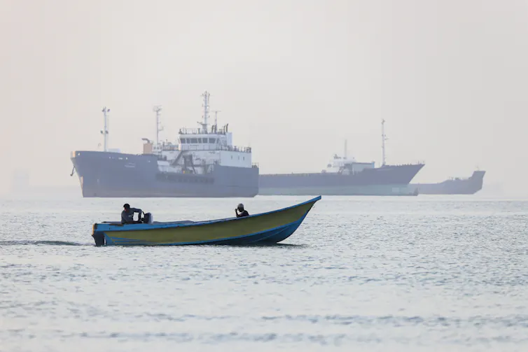 Iranian fishermen steering a boat past ships stuck in the Strait of Hormuz.