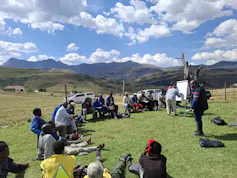 A group of researchers and farmers sit outside in the mountains