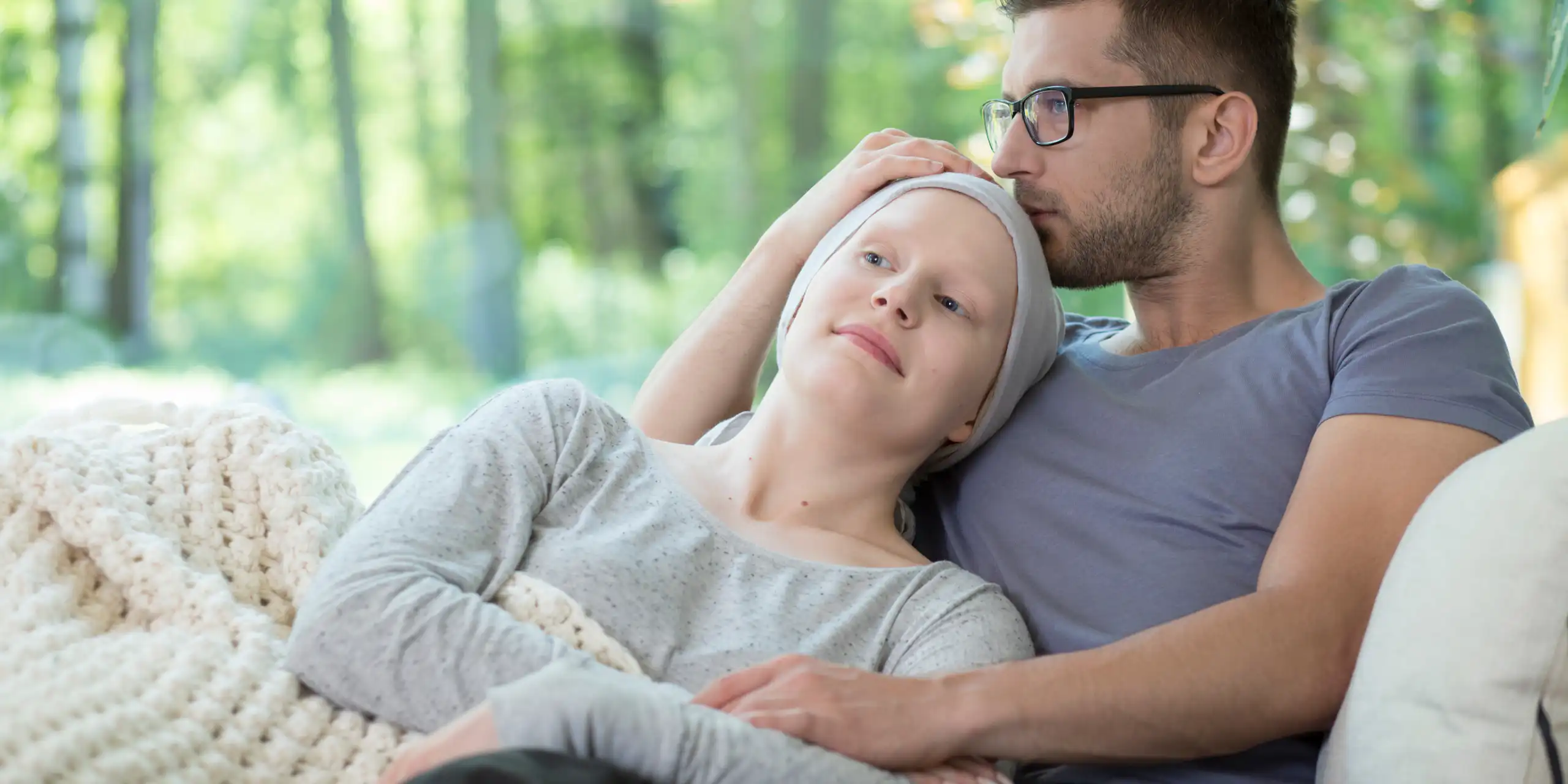 Un homme enlace une femme qui semble malade sur un canapé.