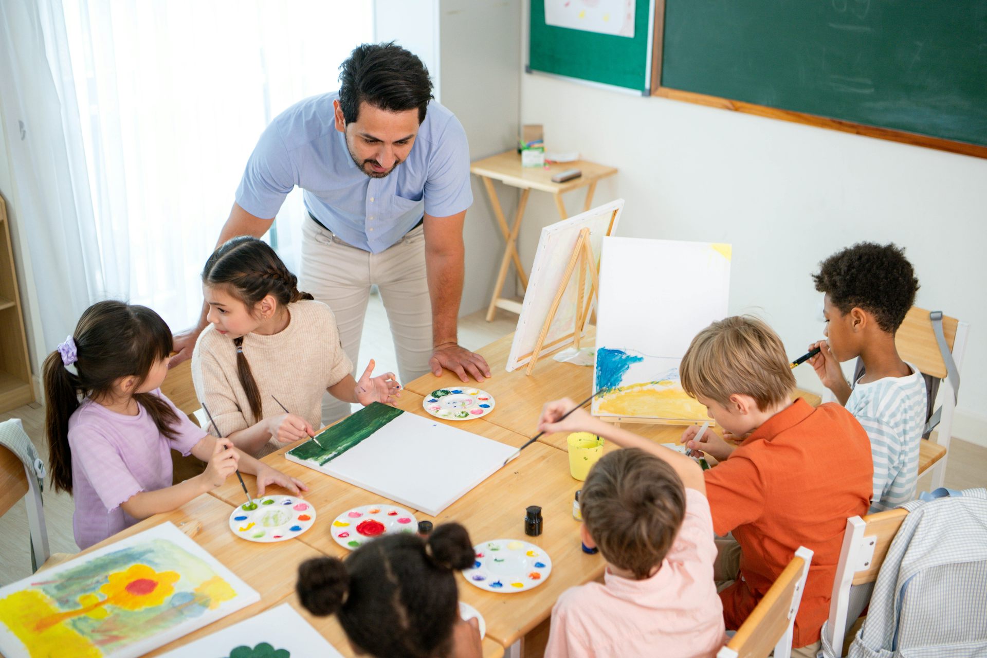 Un mestre dona una classe a infants asseguts pintant.