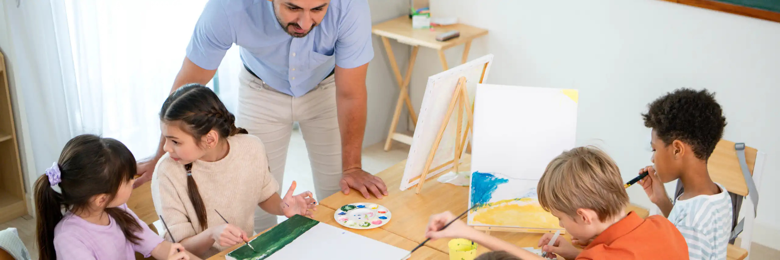 Un mestre dona una classe a infants asseguts pintant.