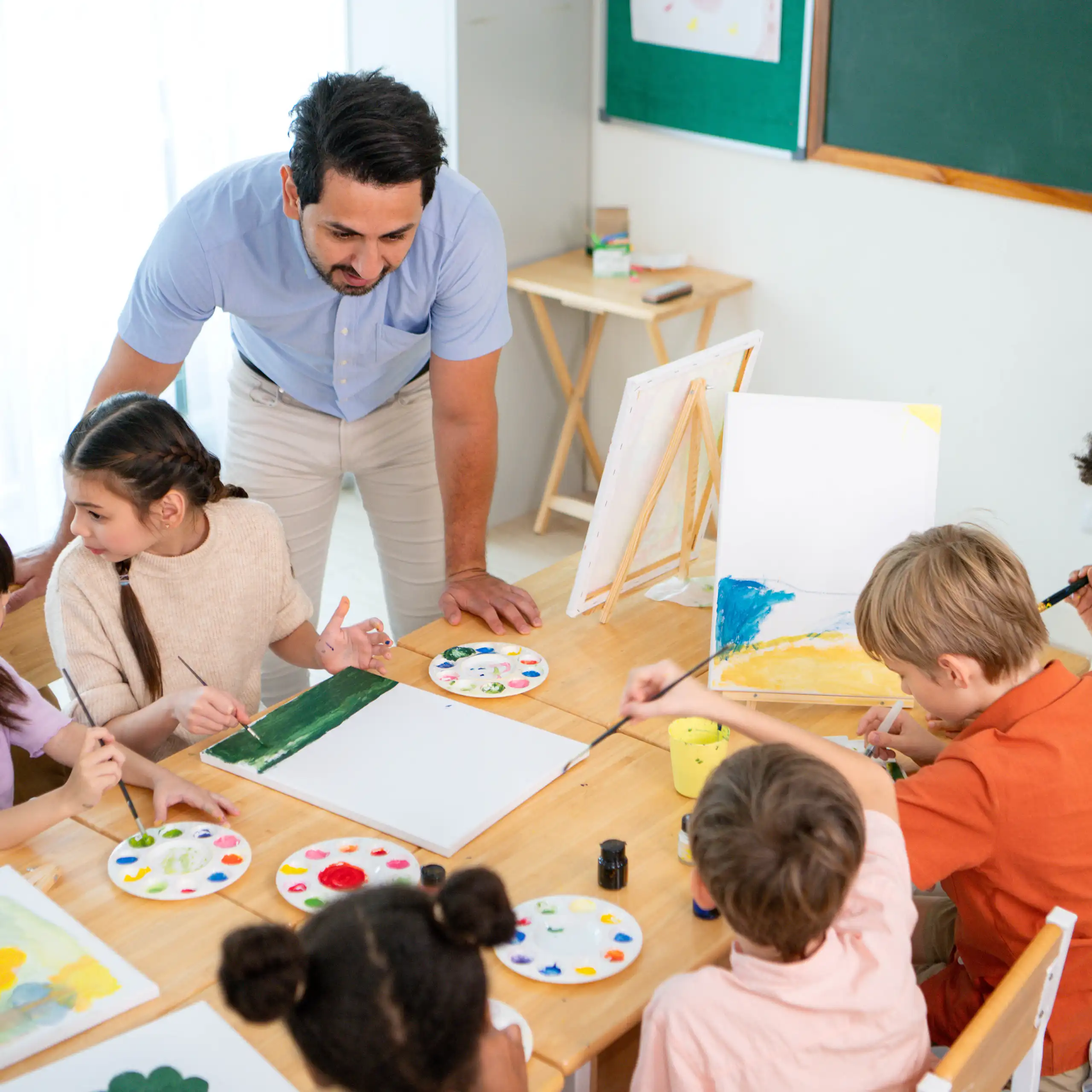 Un mestre dona una classe a infants asseguts pintant.