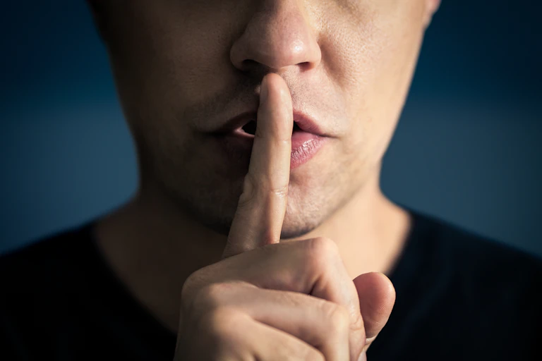 Un hombre se pone el dedo en los labios en ademán de mandar que se guarde silencio.