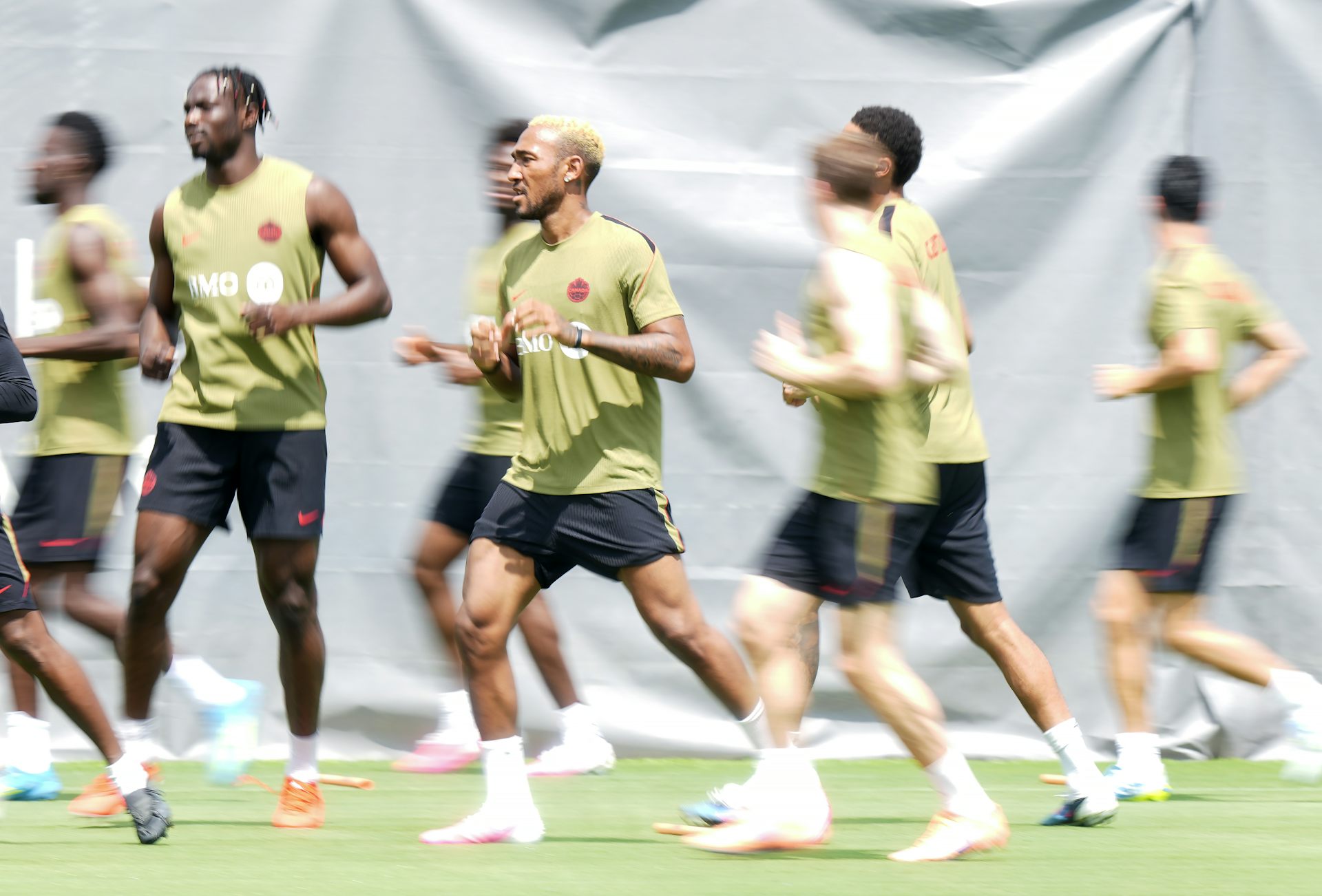 Half a dozen men in green and black athletic gear warm up on a grass field