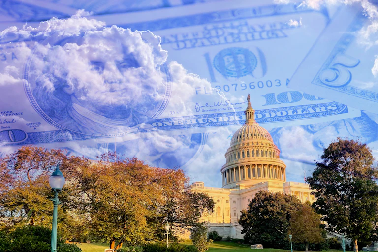 Congress, from a distance, is seen against a blue sky that has outlines of dollar bills imposed onto it in a graphic image.