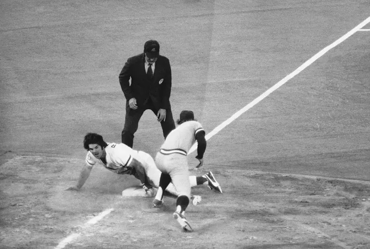 Baseball player slides into base as another player tried to tag him out and umpire watches