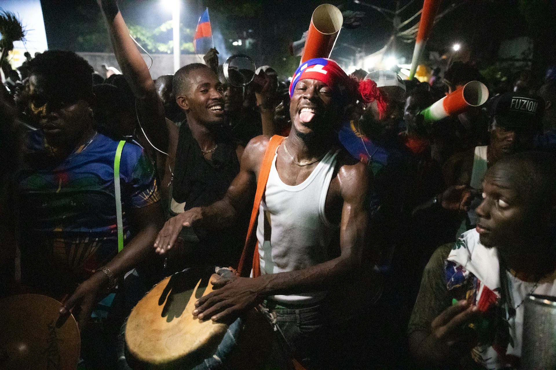 A man beats a drum surrounded by pther people