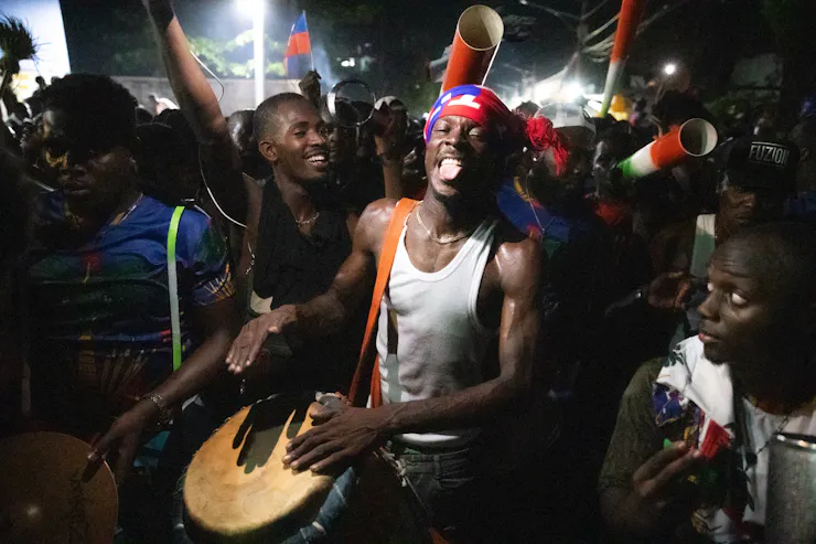 A man beats a drum surrounded by pther people