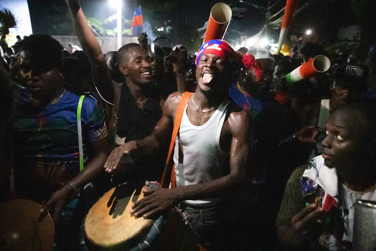A man beats a drum surrounded by pther people
