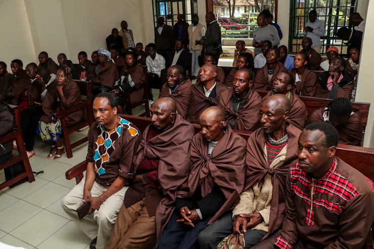 People in traditional clothing sit in chairs in a crowded meeting room.