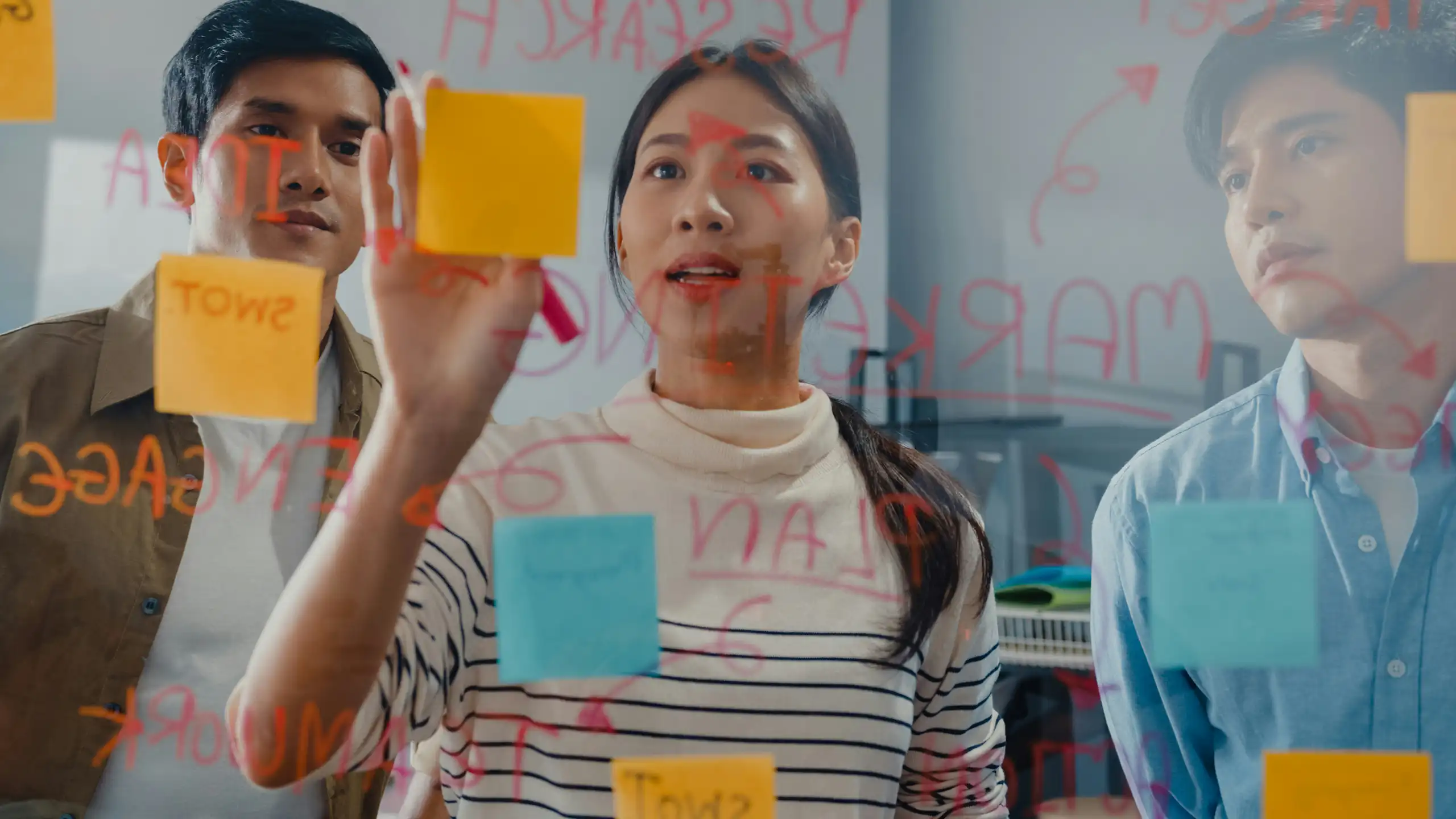 People using post-it notes and dry markers on a glass partition