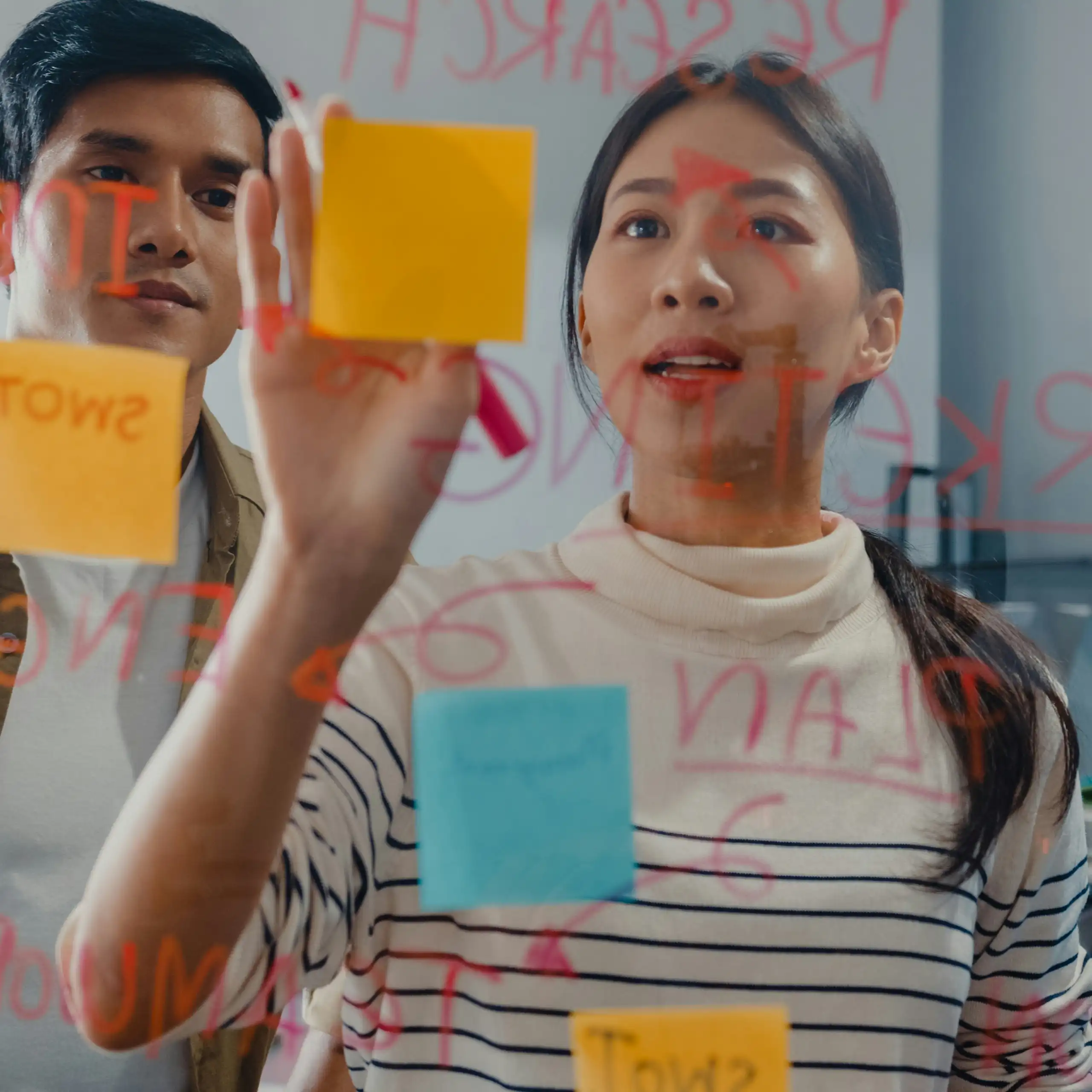 People using post-it notes and dry markers on a glass partition
