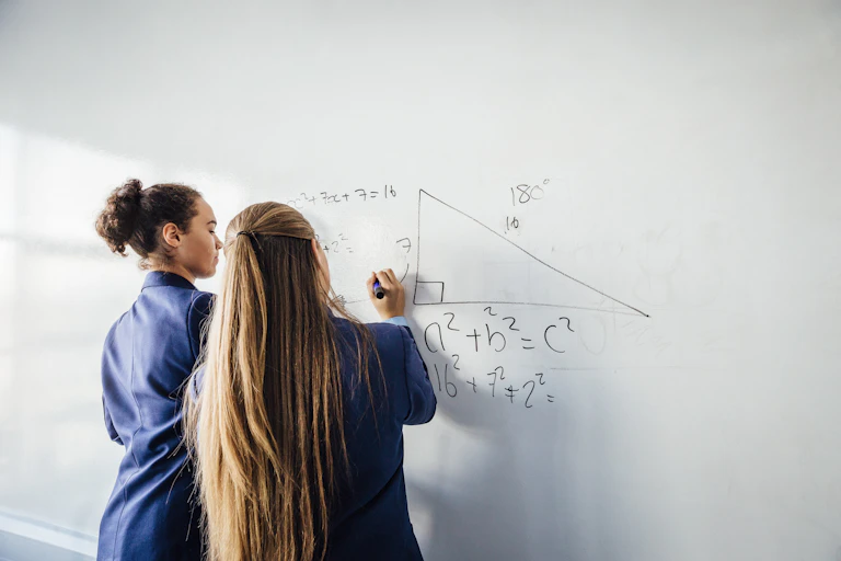 Two teenage students in uniforms solve a maths problem on a whiteboard.