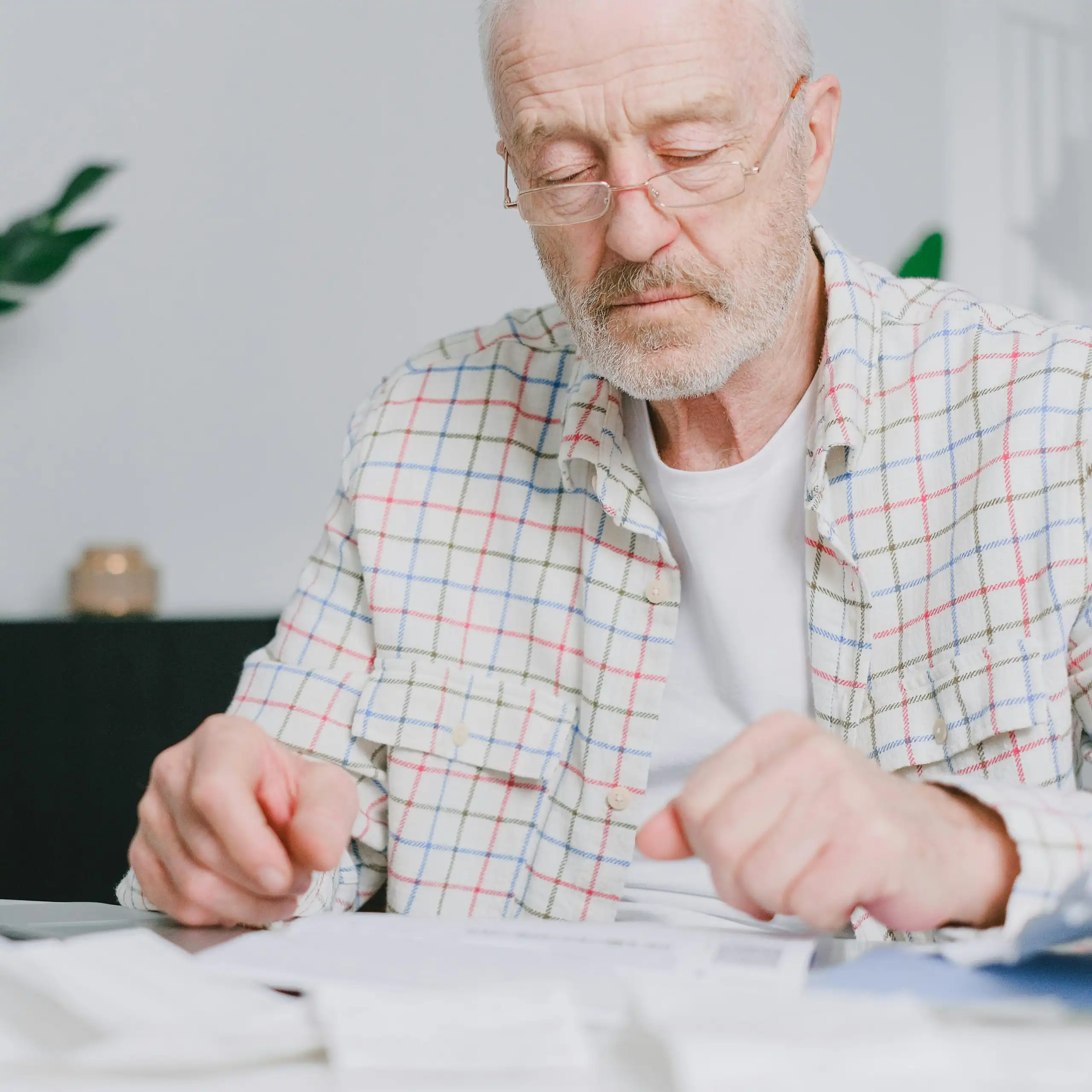 Elderly man with eyeglasses focused on paperwork at home, using laptop