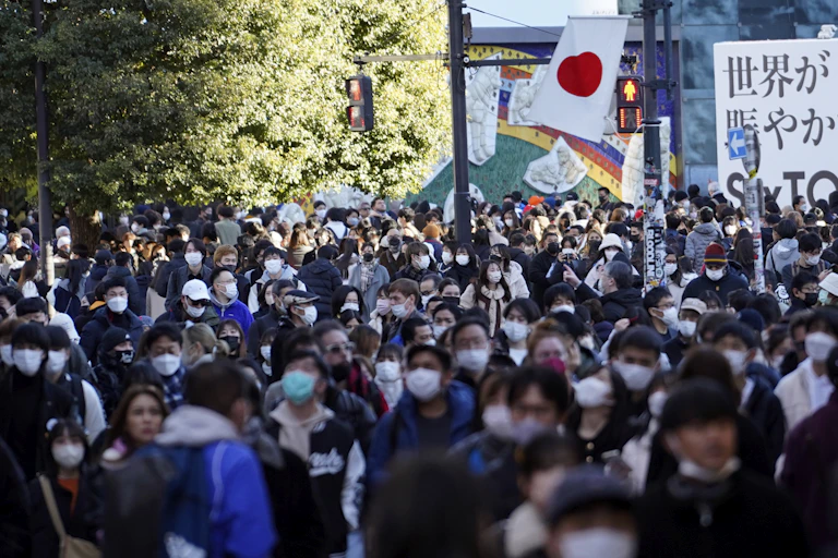 Crowd of people wearing face masks outdoors with Japanese flag visible in the background