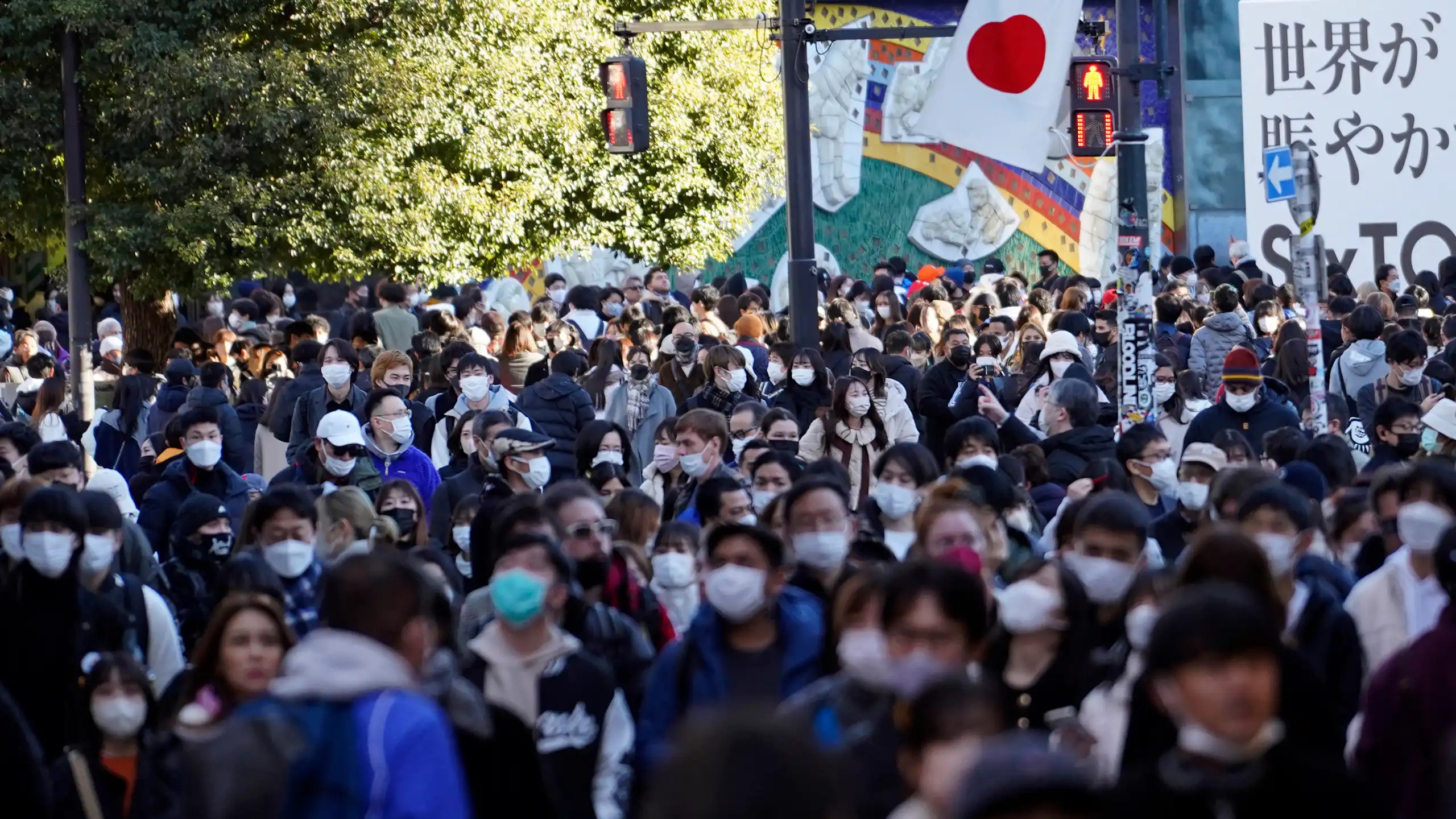 Crowd of people wearing face masks outdoors with Japanese flag visible in the background