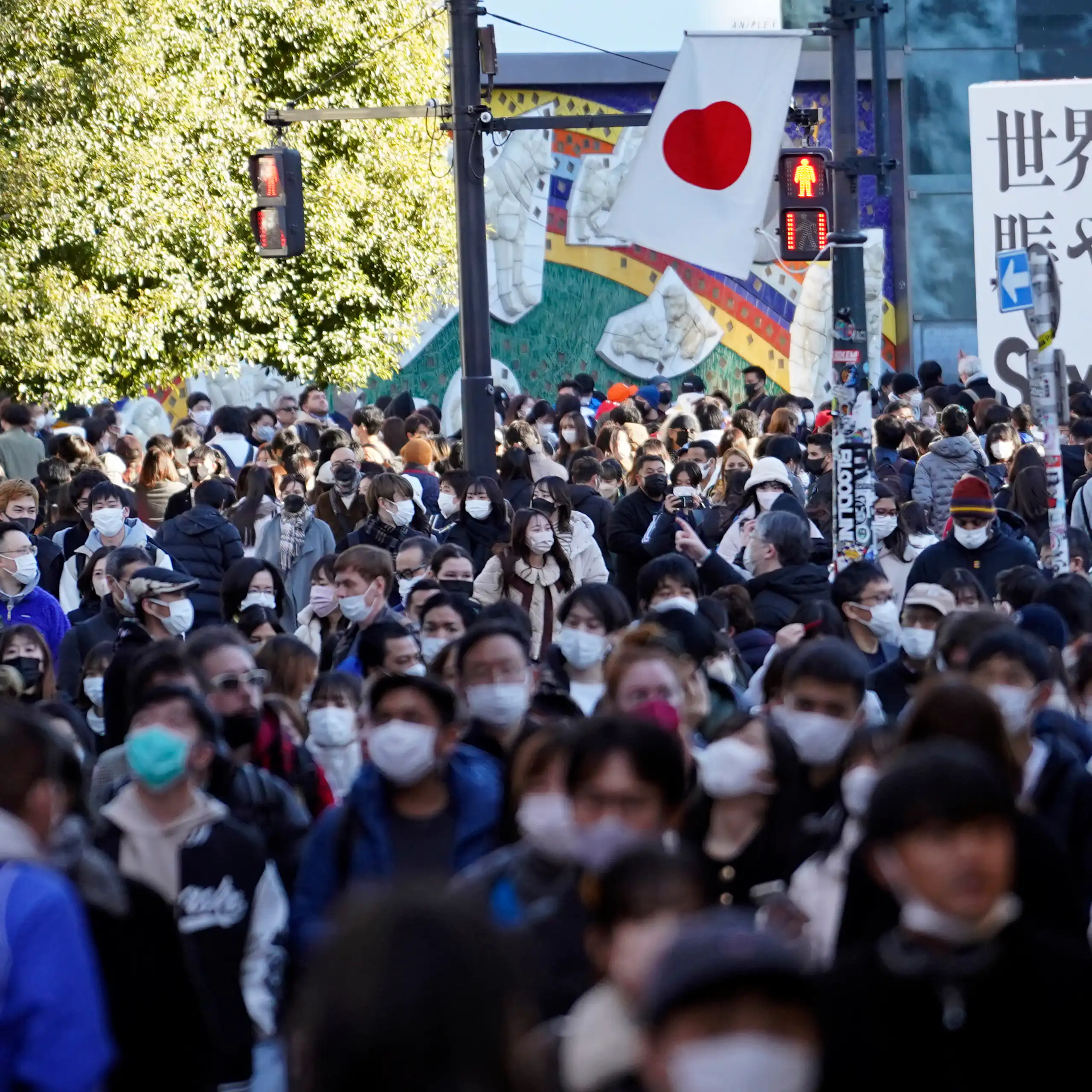 Crowd of people wearing face masks outdoors with Japanese flag visible in the background