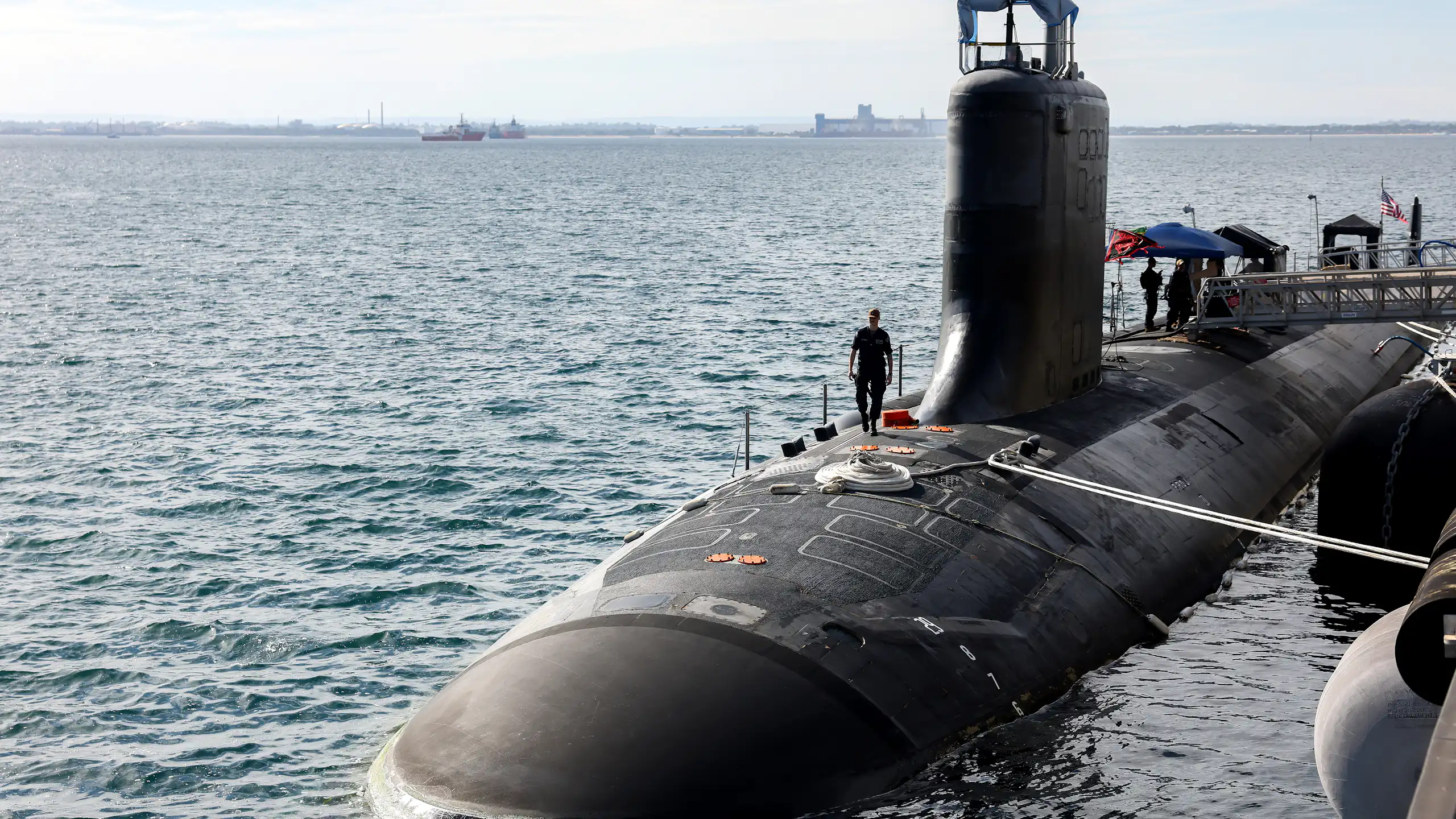 A submarine half submerged in the ocean with a naval office walking on top
