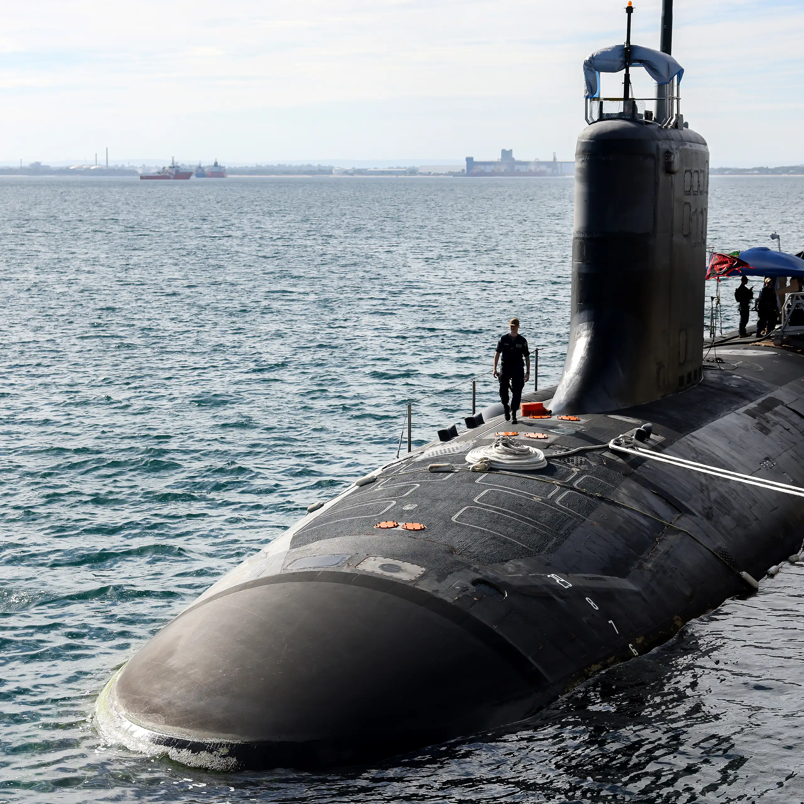 A submarine half submerged in the ocean with a naval office walking on top