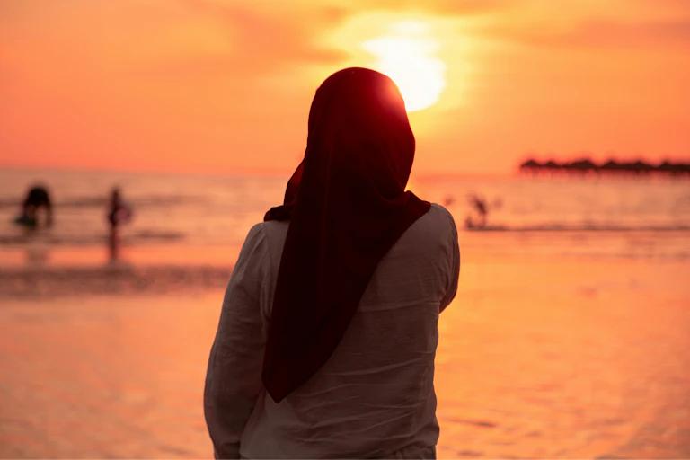 A woman in a hijab is cast in silhouette against a sunset.