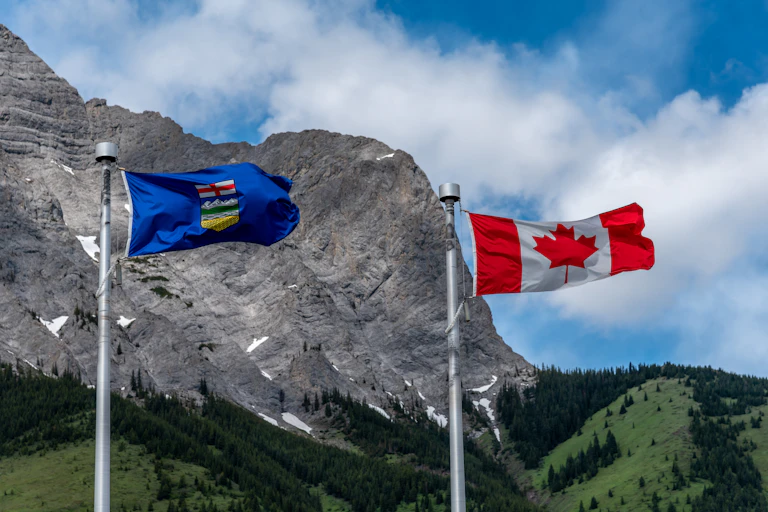The Albertan and Canadian flags fly next to each other in front of mountains.