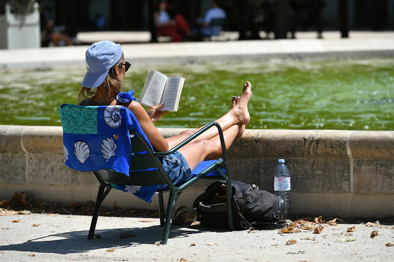 Mujer joven leyendo un libro al borde de una fuente en el jardín del Palais Royal en París, Francia.