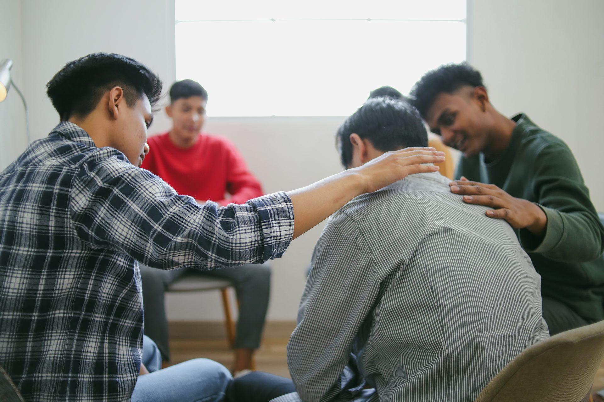 A group of young men sitting in a circle talking, one comforting another