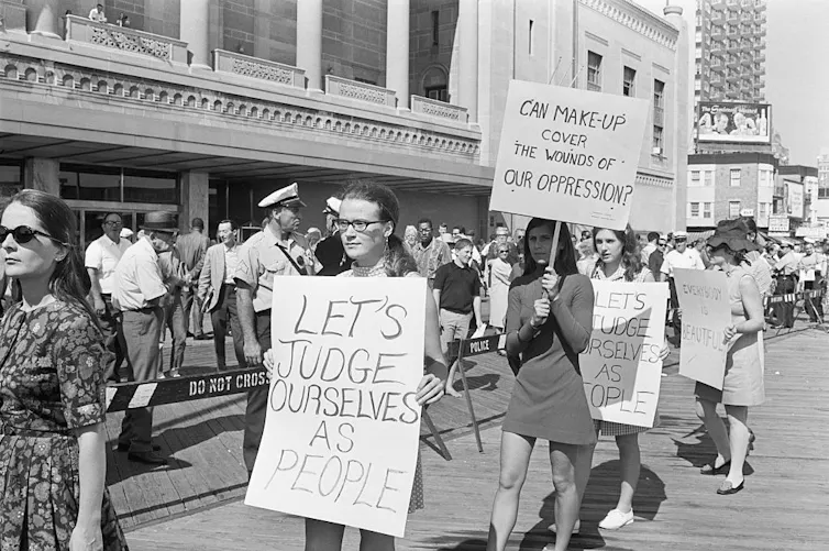 Women march and hold signs, including one that reads 'Can make-up cover the wounds of our opression?'