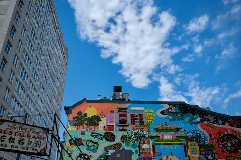 A brightly coloured mural on the side of a small building next to skyscrapers.